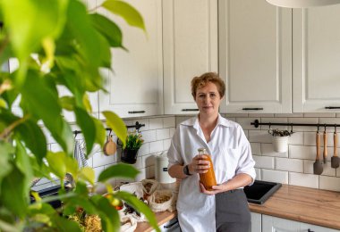 Yetişkin bir kadın elinde balkabağı suyuyla mutfakta duruyor. Doğal ürünlerin ekolojik alımları. Uzayı kopyala Sıfır atık. Plastik yok.