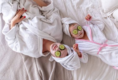 Anne ve kızı yüzlerinde maskeyle yatakta yatıyorlar. Giysiler beyaz kaftandır. Ailedeki hemşire iletişimi. Refah kavramı.