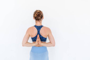 Genç kızıl saçlı kadın arkasında namaste ile yoga yapıyor. Mavi spor kıyafetlerle egzersiz. Beyaz stüdyo dairesi. Uzayı kopyala Refah kavramı.