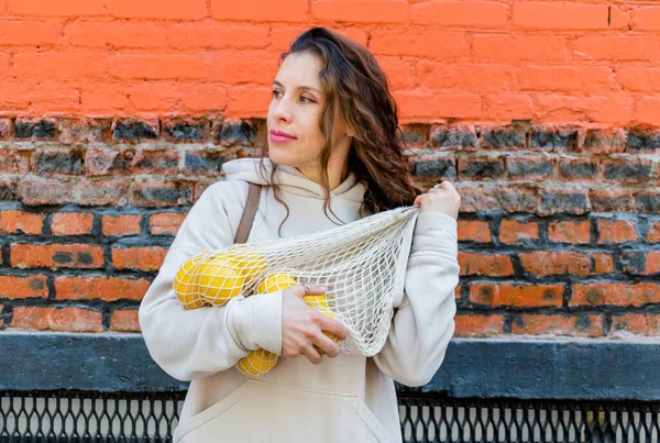 Adult woman in beige suit holds eco friendly cotton bag filled with citrus fruits. Zero waste. Wellness concept.