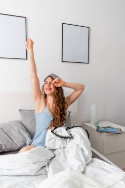 İpek pijamalı genç kadın rahat bir yatakta otururken esniyor. Evim gibi. Sağlık konsepti. Boşluğu kopyala
