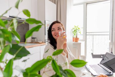 Beyaz cüppeli, siyah saçlı genç bir kadın mutfaktaki sandalyede oturuyor. Eller bardağı meyve suyuyla tutsun. Sağlık ve sağlıklı gıda konsepti