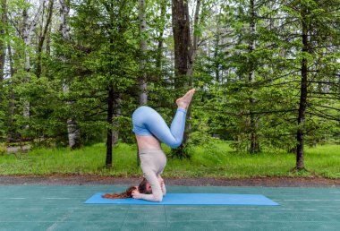 Samimi kızıl saçlı bir kadın parkta yoga yapıyor. Spor giyim ve yoga minderi. Sağlık ve spor yaşam tarzı konsepti. Boşluğu kopyala