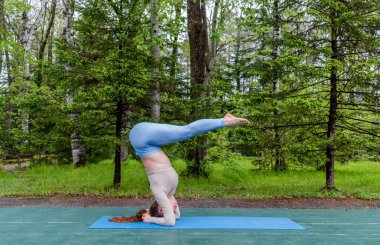 Samimi kızıl saçlı bir kadın parkta yoga yapıyor. Spor giyim ve yoga minderi. Sağlık ve spor yaşam tarzı konsepti. Boşluğu kopyala