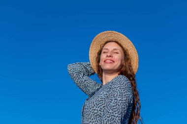 Mavi elbiseli ve hasır şapkalı yetişkin bir kadın nehir kenarında yürüyor. Kırkıncı kişi. Doğada refah ve meditasyon kavramı.