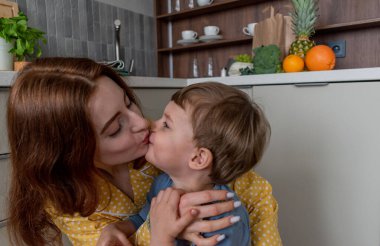 Genç anne küçük oğluna mutfakta sarılıyor. Evin içinde aile sağlığı var. Sabahları sağlıklı kahvaltı konsepti