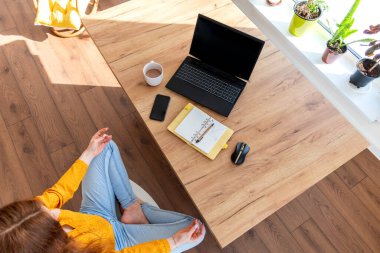 Genç iş kadını işten sonra internetten bilgisayar kullanarak meditasyon yapıyor. Dişi kız dizüstü bilgisayarın yanında sakin müzik dinler. Ev konforu ve ruh sağlığı konsepti.