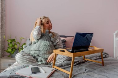 Genç iş kadını, işten sonra internette bilgisayar kullanarak yatakta otururken meditasyon yapıyor. Kız dizüstü bilgisayarın yanında sakin müzik dinliyor. Ev konfor bölgesi ve sağlık konsepti.