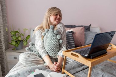 Genç iş kadını, işten sonra internette bilgisayar kullanarak yatakta otururken meditasyon yapıyor. Kız dizüstü bilgisayarın yanında sakin müzik dinliyor. Ev konfor bölgesi ve sağlık konsepti.