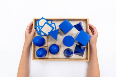 Kızların elinin en üst görüntüsü, Montessori okulundaki renkli ahşap geometrik şekiller bulmacasını çözmek ve oynamaktır. Matematiksel geometri kullanma kavramı çocuk eğitimi için kaynak öğrenme kavramı.