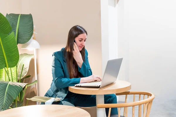 Businesswoman in suite is working online by using computer and talking on phone. Female freelancer browsing in laptop. Concept of remotely working. Technology and people. Networking business.