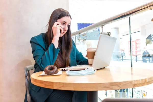 Businesswoman in suite is working online by using computer and talking on phone. Female freelancer browsing in laptop. Concept of remotely working. Technology and people. Networking business.