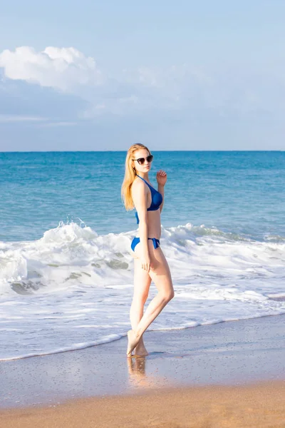 Mulher bonita em biquíni sexy em pé na praia do mar usando óculos de sol — Fotografia de Stock