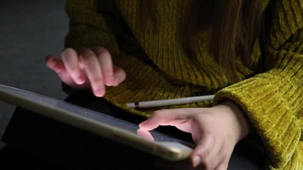 Close-up de mãos femininas digitando informações de texto em um tablet digital enquanto está sentado em uma sala escura. — Vídeo de Stock