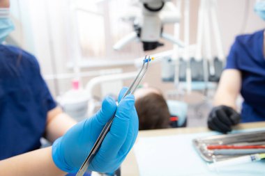 Diş hekimi diş kanallarını tedavi etmek için bir aletle elinde cımbız tutar.