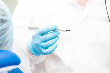 Dişçinin elinde neşter. Diş implantasyonu ameliyatı.