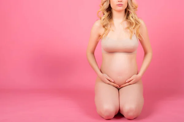 Bela jovem grávida sentada no chão, em um fundo de estúdio rosa — Fotografia de Stock