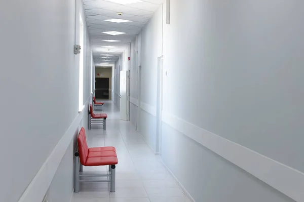 Tomma moderna sjukhus korridor, klinik hall interiör bakgrund med röda stolar för patienter som väntar på läkarbesök. Samtida väntrum på läkarmottagningen. — Stockfoto