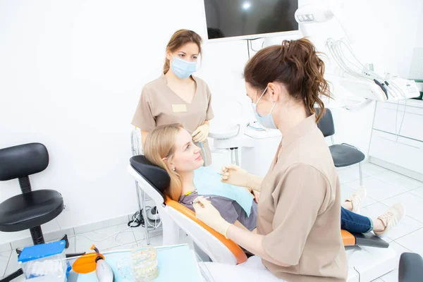 Пациент с дантистом и зубным ассистентом в масках и перчатках. — стоковое фото