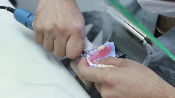 Professionele tandtechnicus of tandarts houden motorhandstuk gereedschap en werken met tandprothese, gebit kunstgebit - close-up bekijken. Stomatologie, geneeskunde, restauratie concept — Stockvideo