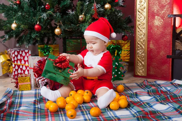 Baby in santa kostuum in de buurt van een kerstboom — Stockfoto