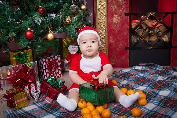 Baby in santa kostuum in de buurt van een kerstboom — Stockfoto