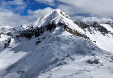 Karlı bir dağ yamacında duran kayakçı. Resmedilmeye değer karla kaplı. Arkaplanda bulutlu mavi bir gökyüzünün altında zirveler. Avusturya Obertauern