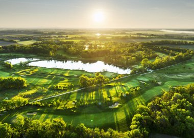 Golf sahası manzarası, yeşil çim yolları ve ormanla dramatik gündoğumunda.