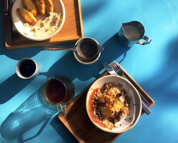 モダンなカフェでブルーを背景においしい健康的な朝食 手製のコーヒーをグラスティーポットに入れます 甘いチーズケーキにキャラメル 太陽の下でテーブルの上のデザイナー料理 昼食の時間だ — ストック写真