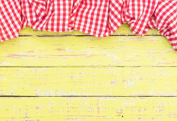 Yellow wooden table surface with rustic red checkered cloth, top view