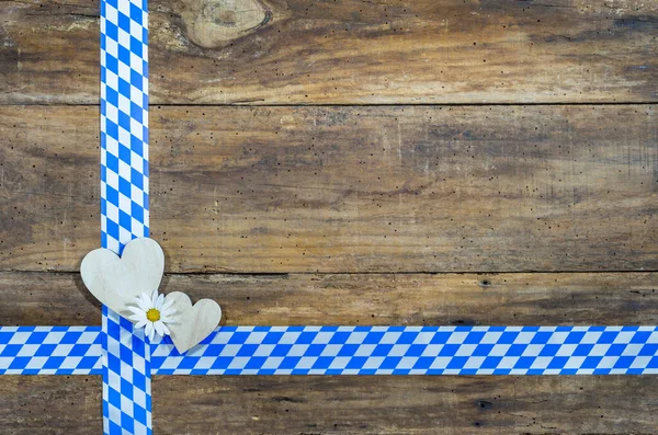 Oktoberfest background with wooden hearts on traditional bavarian blue white pattern border on rustic wooden table background. Copy space