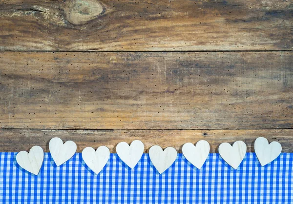 Bavaria or Oktoberfest background with wooden hearts border on blue white checkered tablecloth on rustic wood. Copy space for text.
