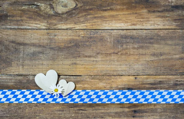 Oktoberfest background with hearts, flower blossom and blue white bavarian border. Copy space for text.