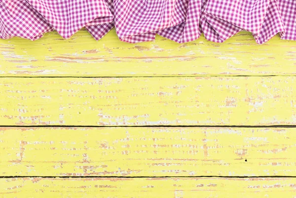 Rustic yellow wooden table surface with purple checkered cloth, top view