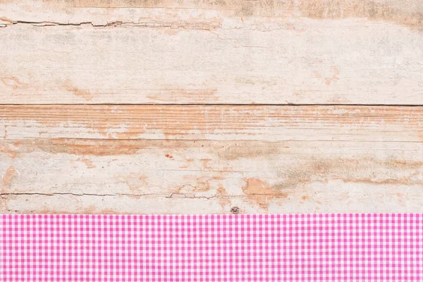 Rustic wooden table surface with pink checkered cloth, top view