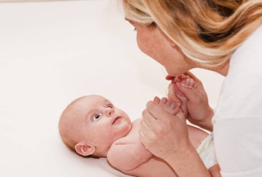 Anne ve çocuk beyaz bir yatakta. Anne, bebek ya da bebek bezli kız güneşli yatak odasında oynuyorlar. Ebeveyn ve küçük çocuk evde dinleniyor. Aile birlikte eğleniyor. Bebek odası için yatak ve tekstil