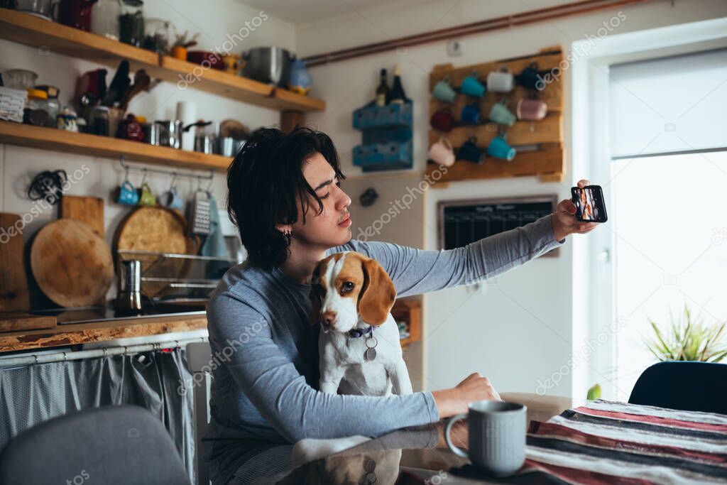 young man with his dog in kitchen at home, morning scene, taking picture
