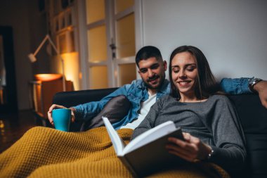 Romantik çift oturma odalarında kanepede uzanıp kitap okuyor.