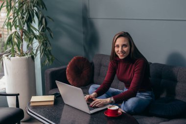 Kadın dizüstü bilgisayar kullanıyor ve evdeki koltukta oturuyor.