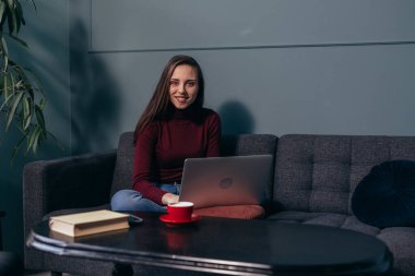 Kadın dizüstü bilgisayar kullanıyor ve evdeki koltukta oturuyor.