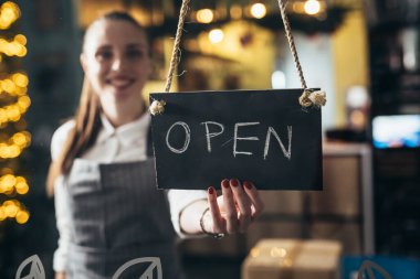Garson kafe ya da restoran açıyor, elinde açık tabela var.