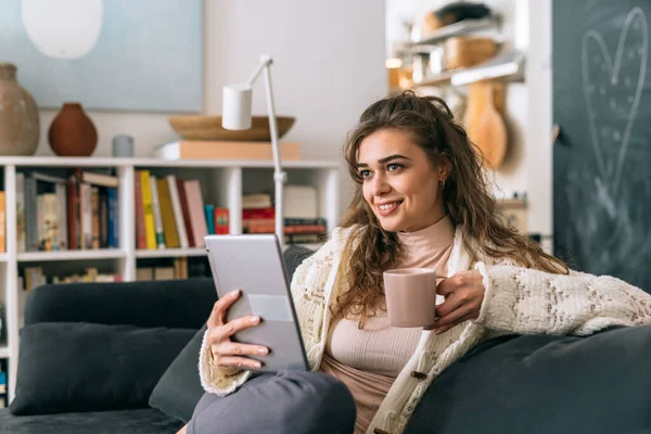 Dijital tablet kullanan bir kadın evdeki oturma odasında kanepede oturuyor.