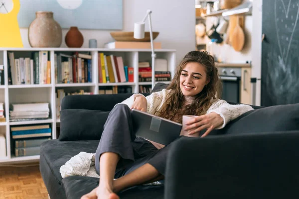 Dijital tablet kullanan bir kadın evdeki oturma odasında kanepede oturuyor.
