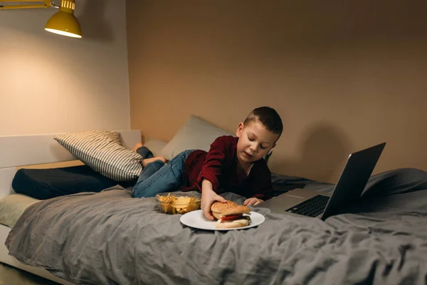 young boy playing games on laptop computer and eating junk food. online games addicted