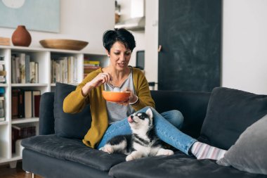 Kadın, oturma odasındaki kanepede otururken köpeğiyle kahvaltı yapıyor.