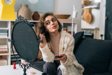 Kadın evinde kanepede otururken makyaj yapıyor.