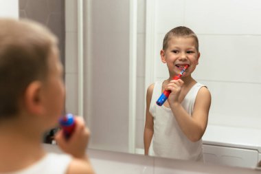 Küçük çocuk banyoda dişlerini fırçalıyor.