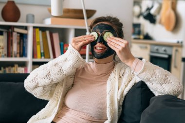 Evindeki kanepede dinlenen bir kadın. Yüzüne estetik maske taktırmış.