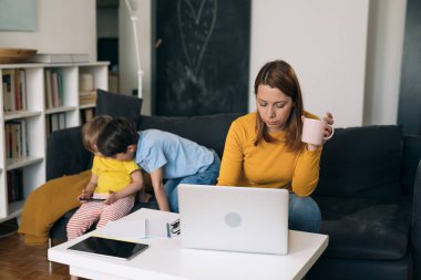 Annem evden laptopla çalışmaya çalışıyor. Çocukları arka planda oynuyor.
