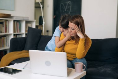 Annem evde çalışıyor. Oğlu ona sarılarak destek oluyor.